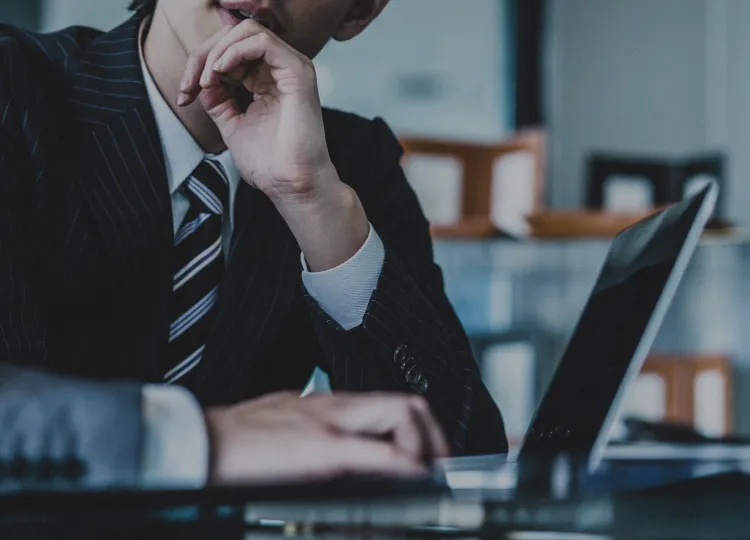 考え込む人物と開いたノートPC